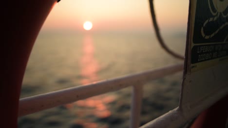 rack focus shot on a vessel cruising the sea on sunset with the sun on the background and a life buoy on the foreground, slow motion, greece