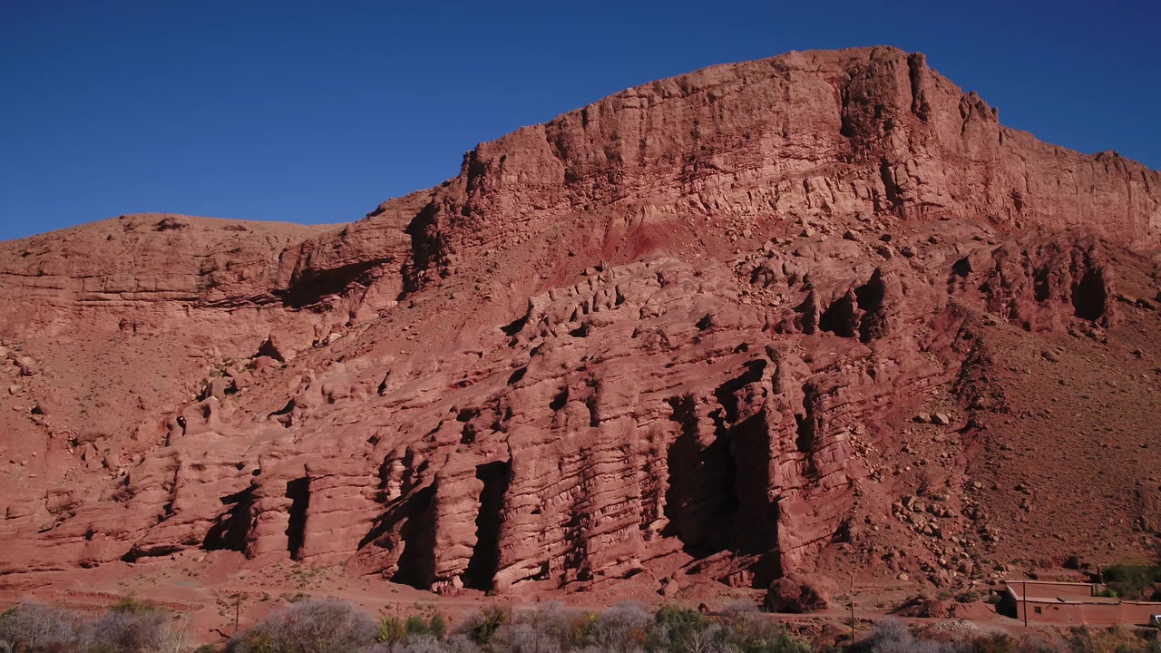 Ripresa aerea con drone che cattura l'imponente parete rocciosa di conglomerato rosso e gli strati rocciosi verticali della formazione Monkey Fingers nella Valle del Dades, Marocco