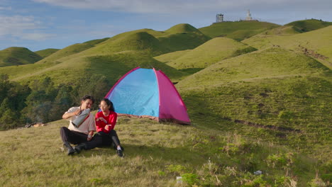 romantic trip to sailung in dolakha, nepal, couple camps in tent after trekking over lush green hills with mountains as a backdrop under clear blue skies, idyllic and romantic environment