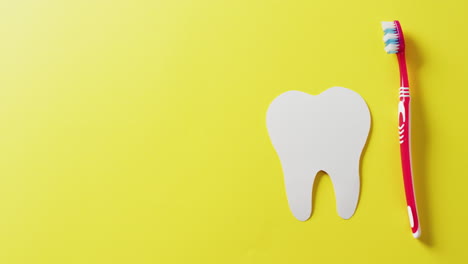 video of white paper tooth and red toothbrush on yellow background with copy space