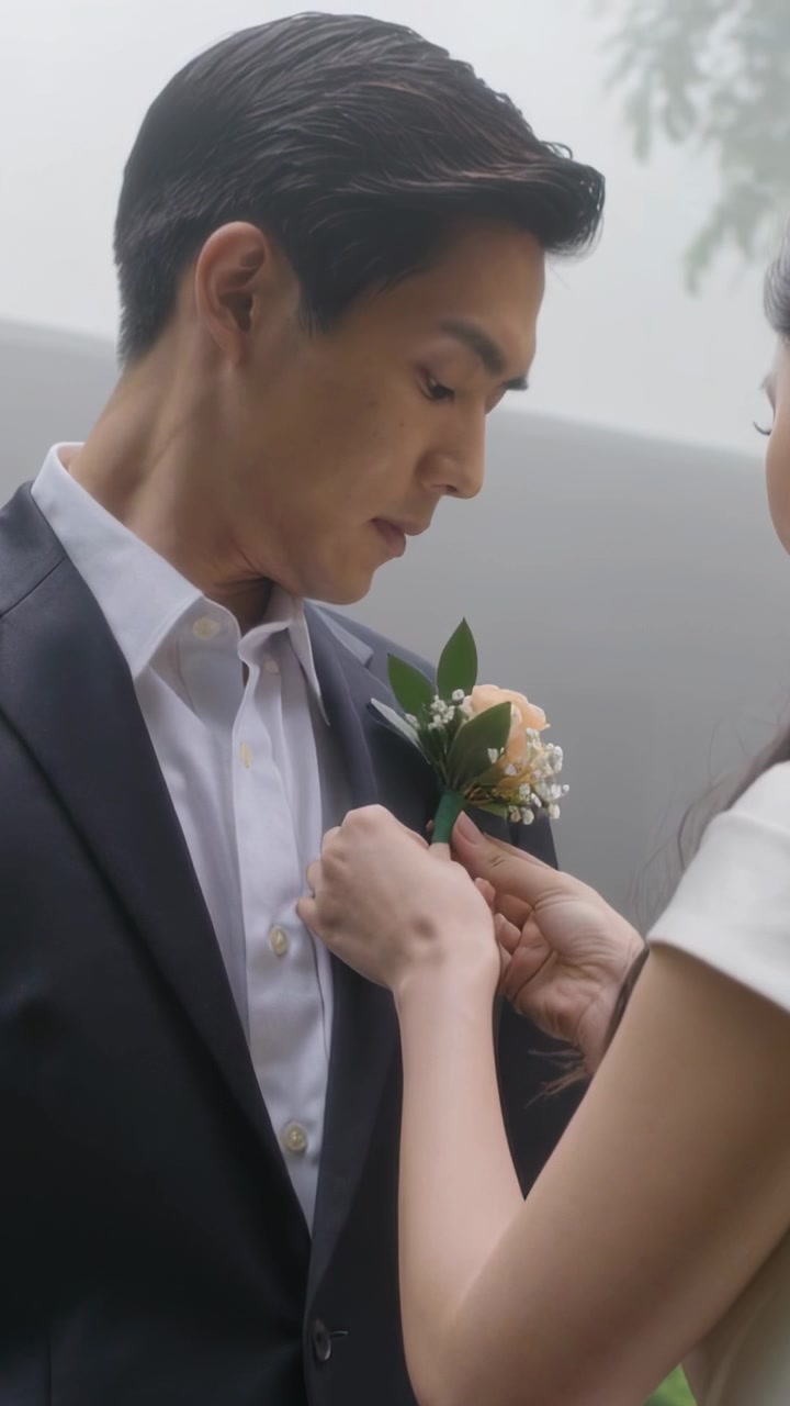 竖屏视频：新娘手持玫瑰，身穿白色婚纱，在公园里为宣誓的新郎别上胸花。