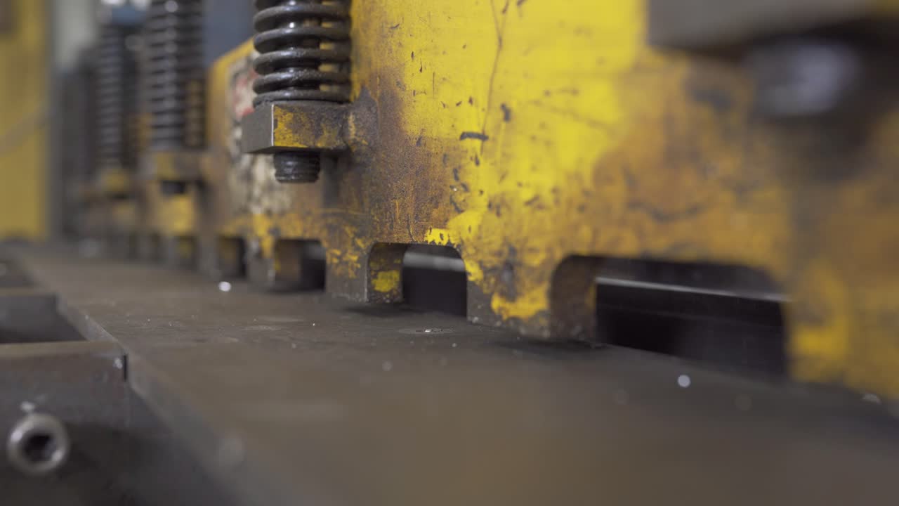 una foto de cerca de una cizalla automática de metal, cortando acero, dentro de una fábrica industrial