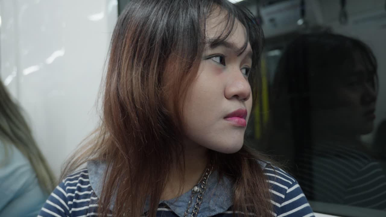 Young indonesian woman with thoughtful expression riding a train, gazing out the window.