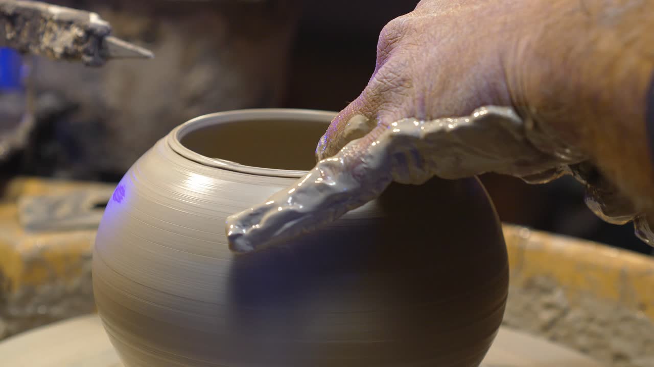 Un artigiano modella un vaso di argilla umida su un tornio. Primo piano delle mani che modellano la forma in ceramica. Artigianato tradizionale della ceramica in un ambiente di laboratorio. Creazione di ceramiche artistiche fatte a mano.
