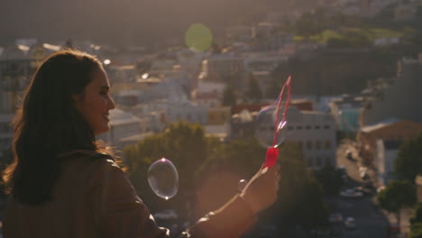 Hermosa-Joven-Caucásica-Soplando-Burbujas-En-La-Azotea-Al-Atardecer-Disfrutando-De-Un-Divertido-Día-De-Verano-Con-La-Ciudad-Al-Fondo