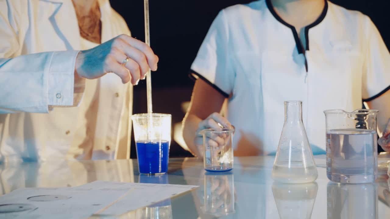Professional chemist in a lab coat is experimenting by mixing liquid chemicals in flasks. Close-up