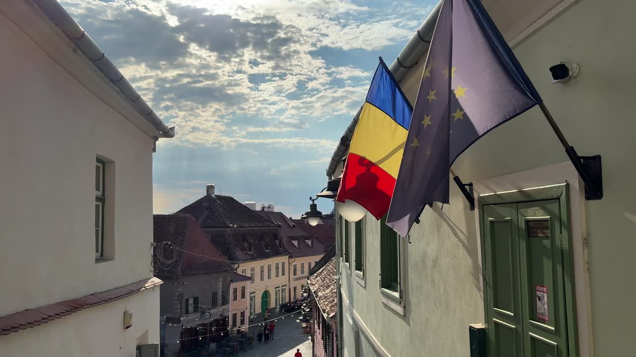 Romanian and EU flags over medieval old town street in summer, static shot