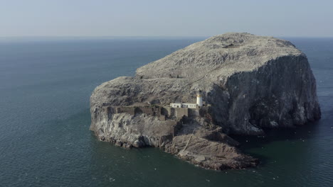 An-aerial-view-circling-Bass-Rock-and-lighthouse-as-gannet-seabirds-circle-their-island-colony-on-a-sunny-day,-East-Lothian,-Scotland