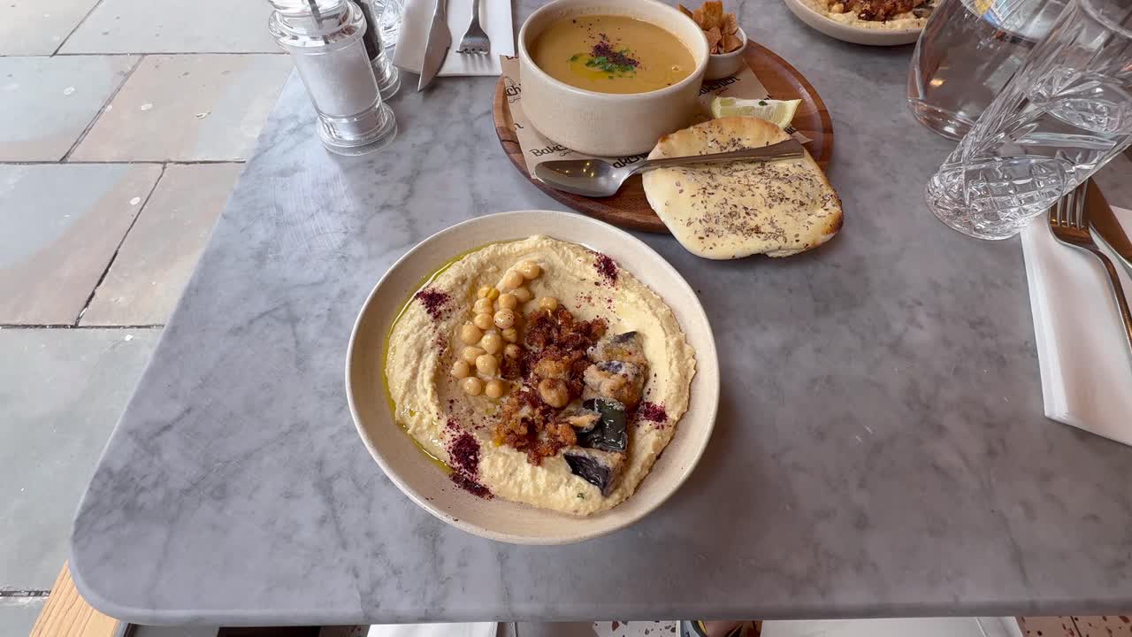 High angle view of Middle Eastern meal on marble table. Shows bowl of hummus with chickpeas and bowl of lentil soup with flatbread. For food or dining content, Liverpool, UK