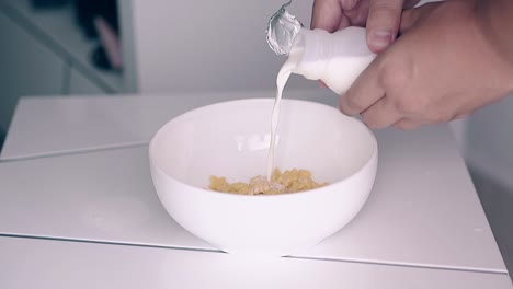 man-pours-milk-from-little-bottle-into-bowl-with-cereals