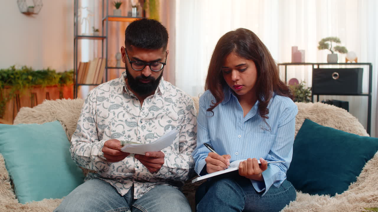 Indian family couple man woman calculating bills money at home making notes reacting frustration