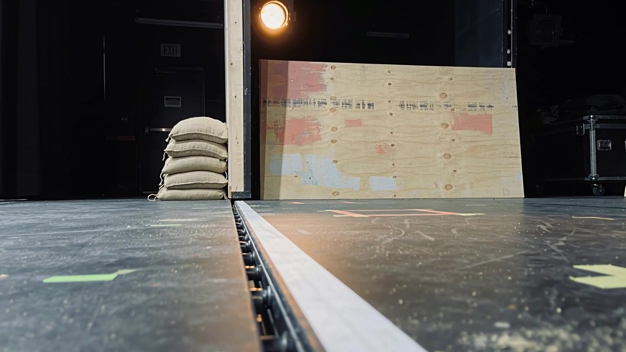 Settling camera, stage seam sliding forward across wing with tape marks, sandbags, plywood