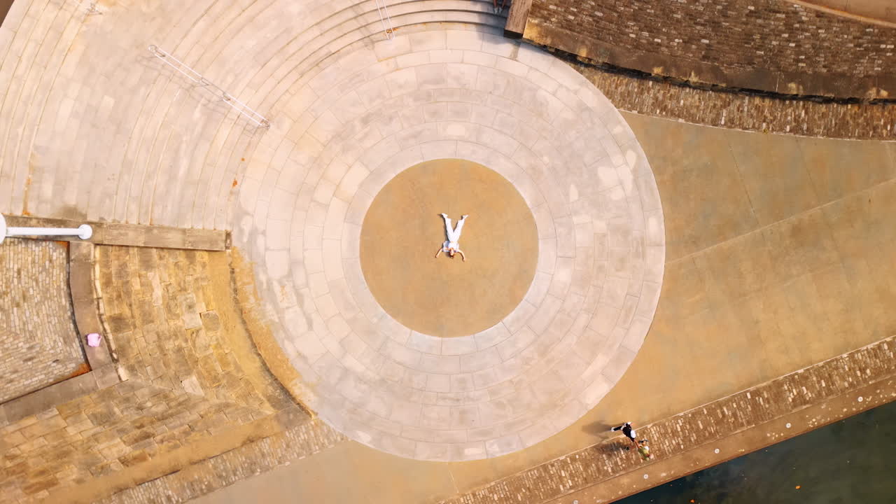Pittsburgh, USA, 2 August 2025: Woman wearing white clothes lies in the center of the circle on the sidewalk. Drone footage rising over the quay of Pittsburg, Pennsylvania, USA