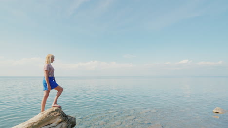 Active-Woman-Traveler-Stands-On-The-Edge-Of-A-Log-Admires-A-Beautiful-View-Of-The-Calm-Sea-And-Blue-