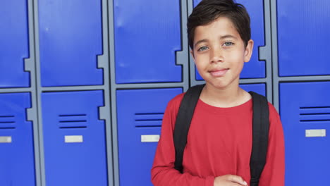 En-El-Pasillo-De-Una-Escuela,-Un-Joven-Estudiante-Birracial-Se-Encuentra-Frente-A-Casilleros-Azules-Con-Espacio-Para-Copiar