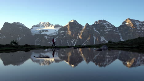 female hikes across the edge of a glacial lake with snow capped mountains