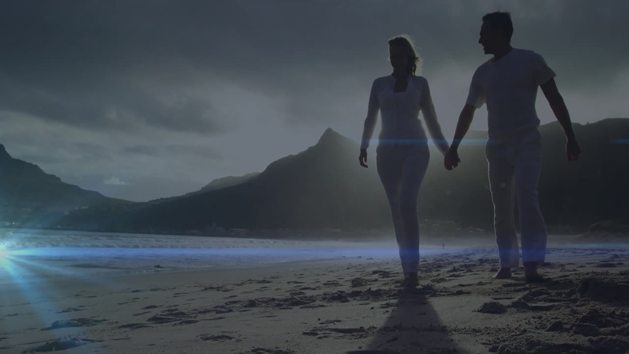 Walking on beach, silhouetted couple with mountains in background at sunset
