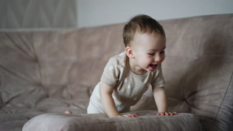 happy active toddler playing hide and seek on the sofa. kid lies down and rises above the pillow and laughs adorably.