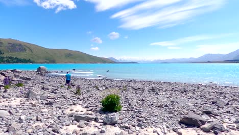 man walking across the shore of lake tekapo with mountains in the background