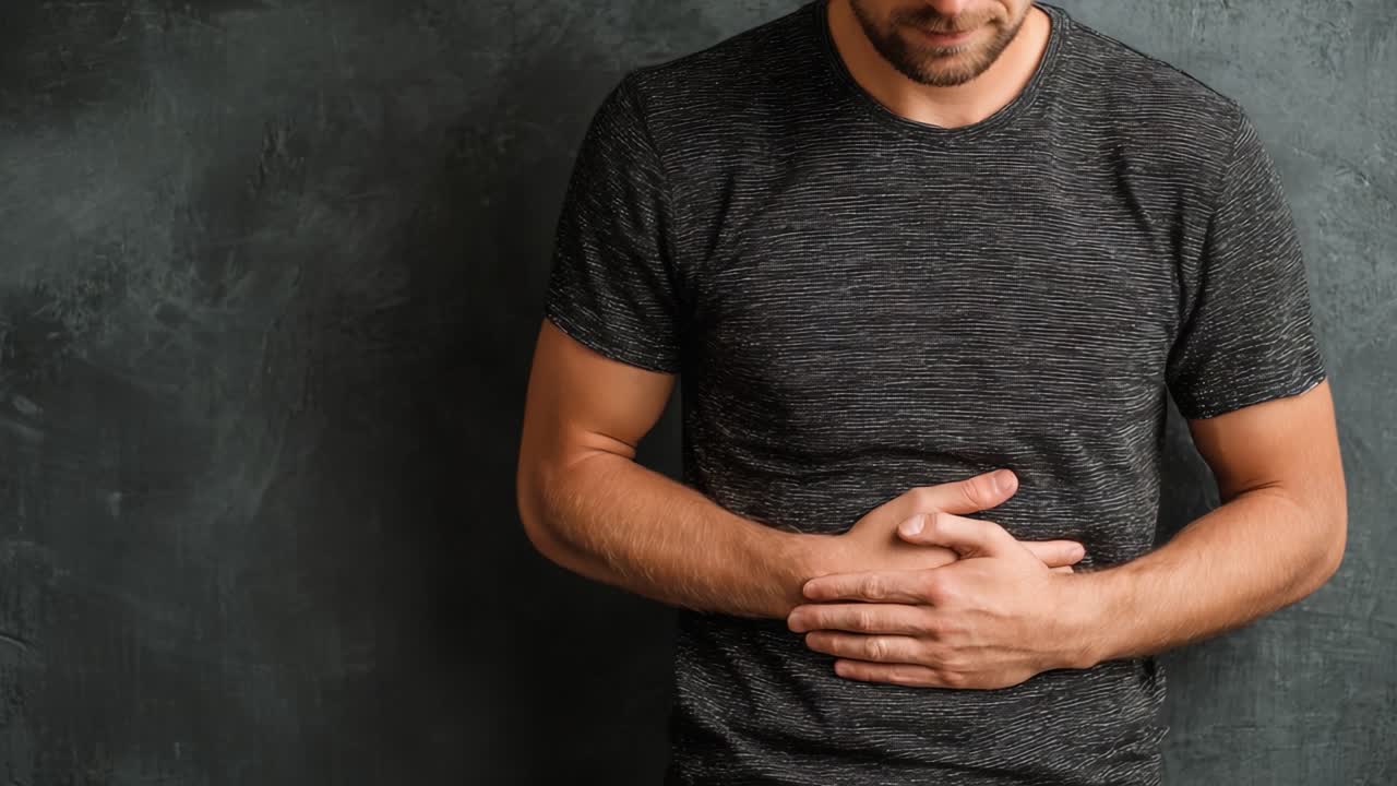 Un uomo si stringe lo stomaco con un'espressione preoccupata, raffigurando disagio o dolore e mostrando sofferenza emotiva e fisica in un ambiente sommesso.