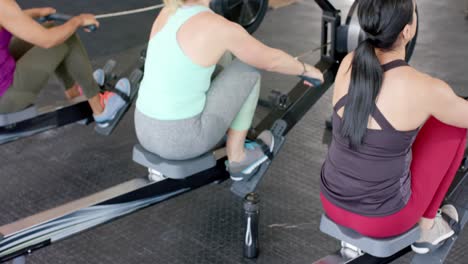 determined unaltered diverse women exercising on rowing machines at gym, in slow motion