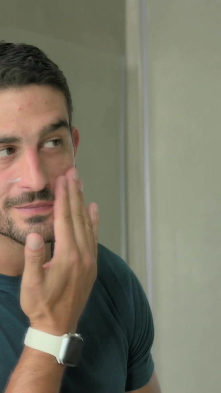 Video verticale: uomo che apre un barattolo, idrata il viso al lavandino, si guarda allo specchio, indossa una maglietta color verde acqua, con spazio per il testo.