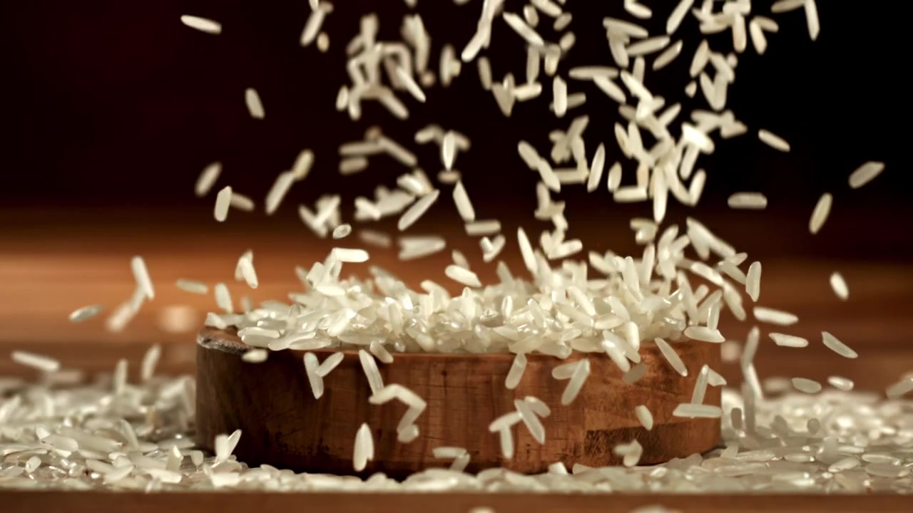 Chicchi di riso bianco che cadono in una ciotola di legno al rallentatore