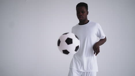 un jugador profesional de fútbol negro con un uniforme blanco sobre un fondo blanco hace malabares con una pelota en cámara lenta. jugador de fútbol de grupo étnico afroamericano con una pelota de fútbol