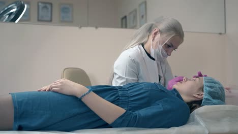 brow master in gloves works with young woman lying on couch