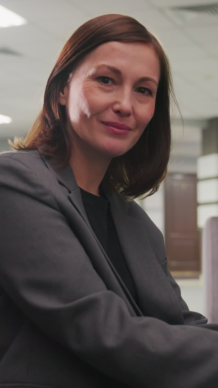 Businesswoman sitting in modern office lounge, massaging her neck in relief. Female professional taking a break from work, looking relaxed and thoughtful in corporate environment