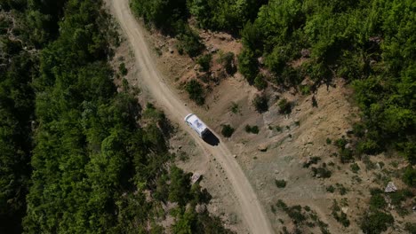 drone footage looking down on a white camper van winding its way along a dirt trail in the trebeshinë-dhëmbel-nemërçkë mountain chain near permet, albania