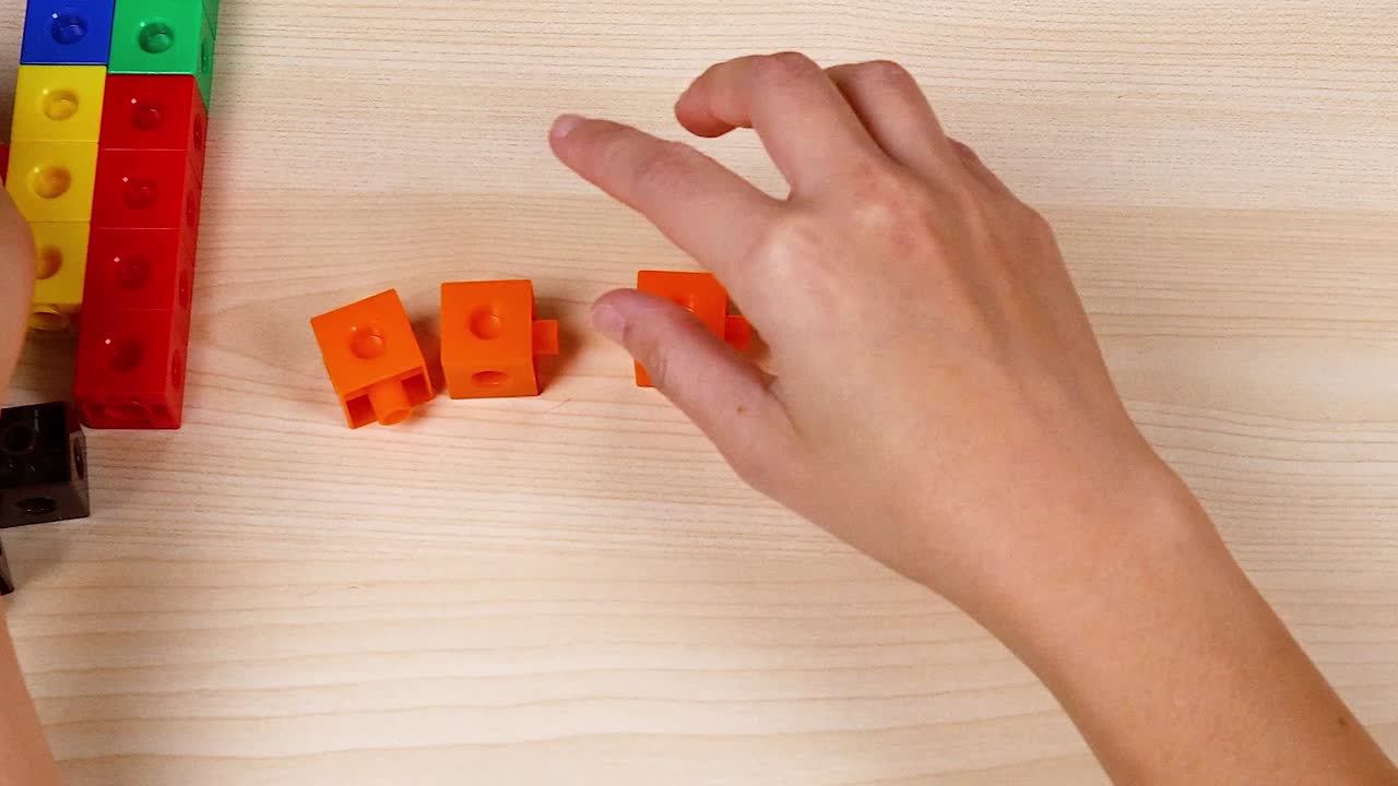 Hands manipulate orange cubes on a wooden table, showcasing creativity and spatial skills.