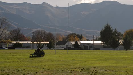 ride-on mower crossing frame on football field in front of mountain range