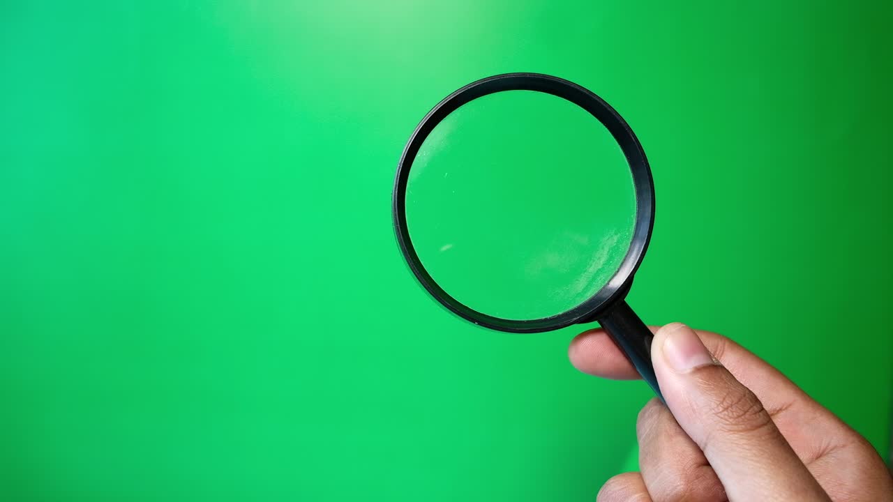 Hand Holding a Magnifying Glass on a Green Background