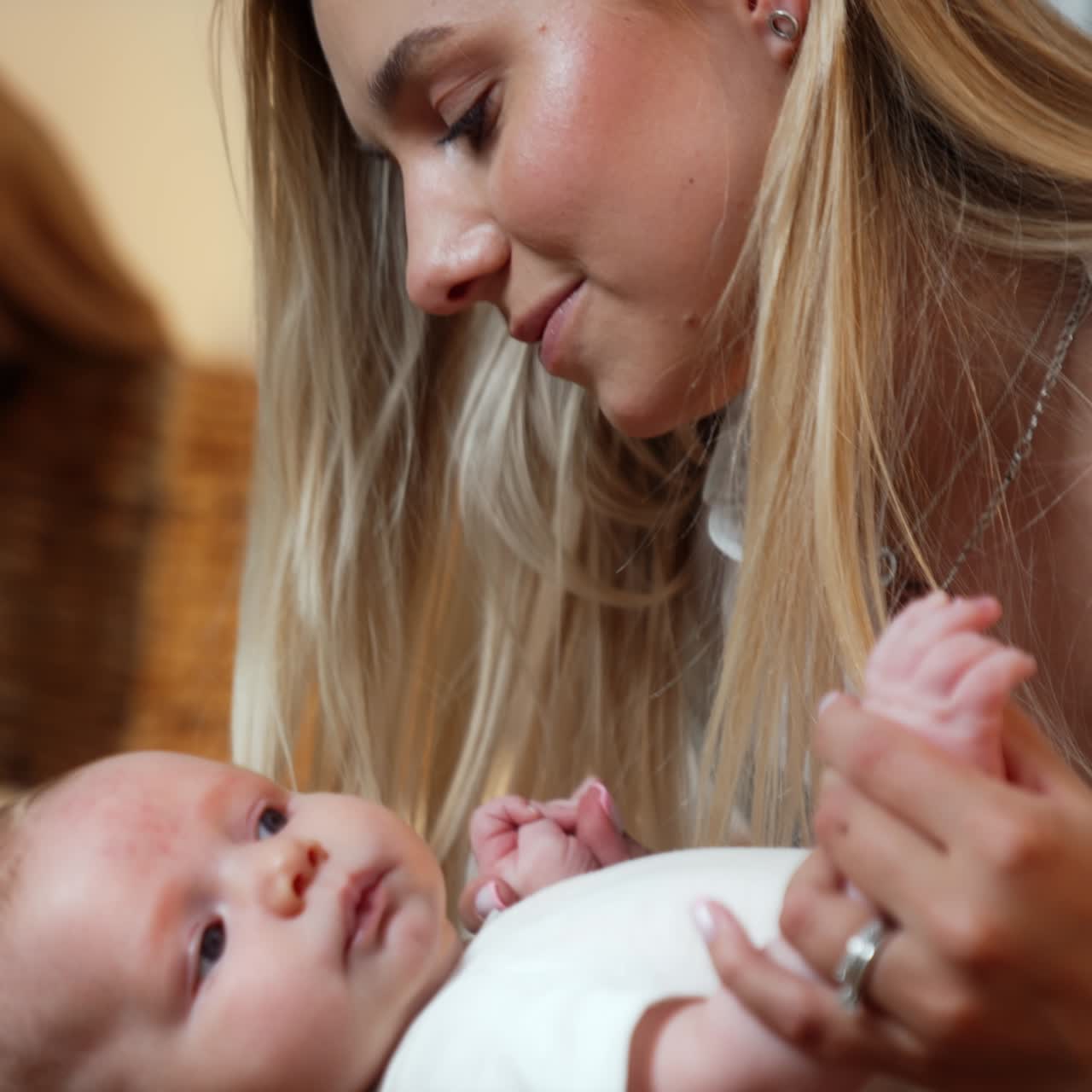Blonde long-haired woman with her newborn baby. Mother leans to her child's face caressing little kid. Close up