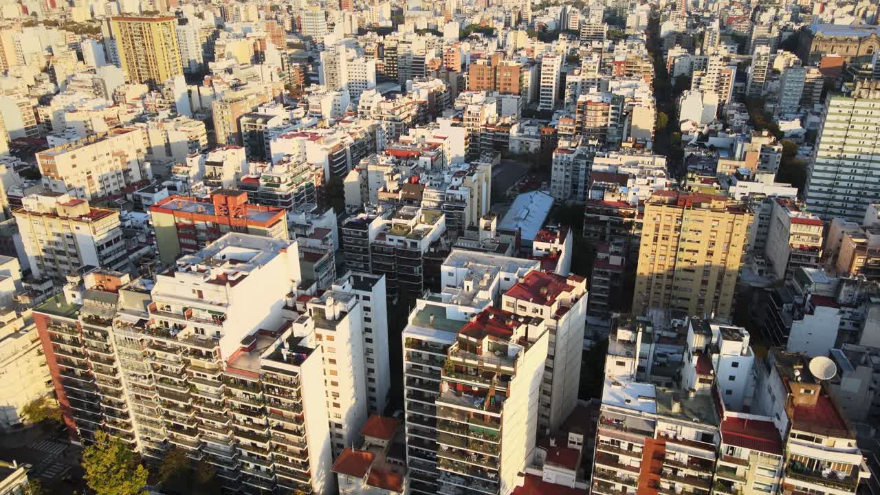 Aerial tilt up from foreground buildings reveals dense cityscape of Buenos Aires near Rivadavia park golden light, Argentina