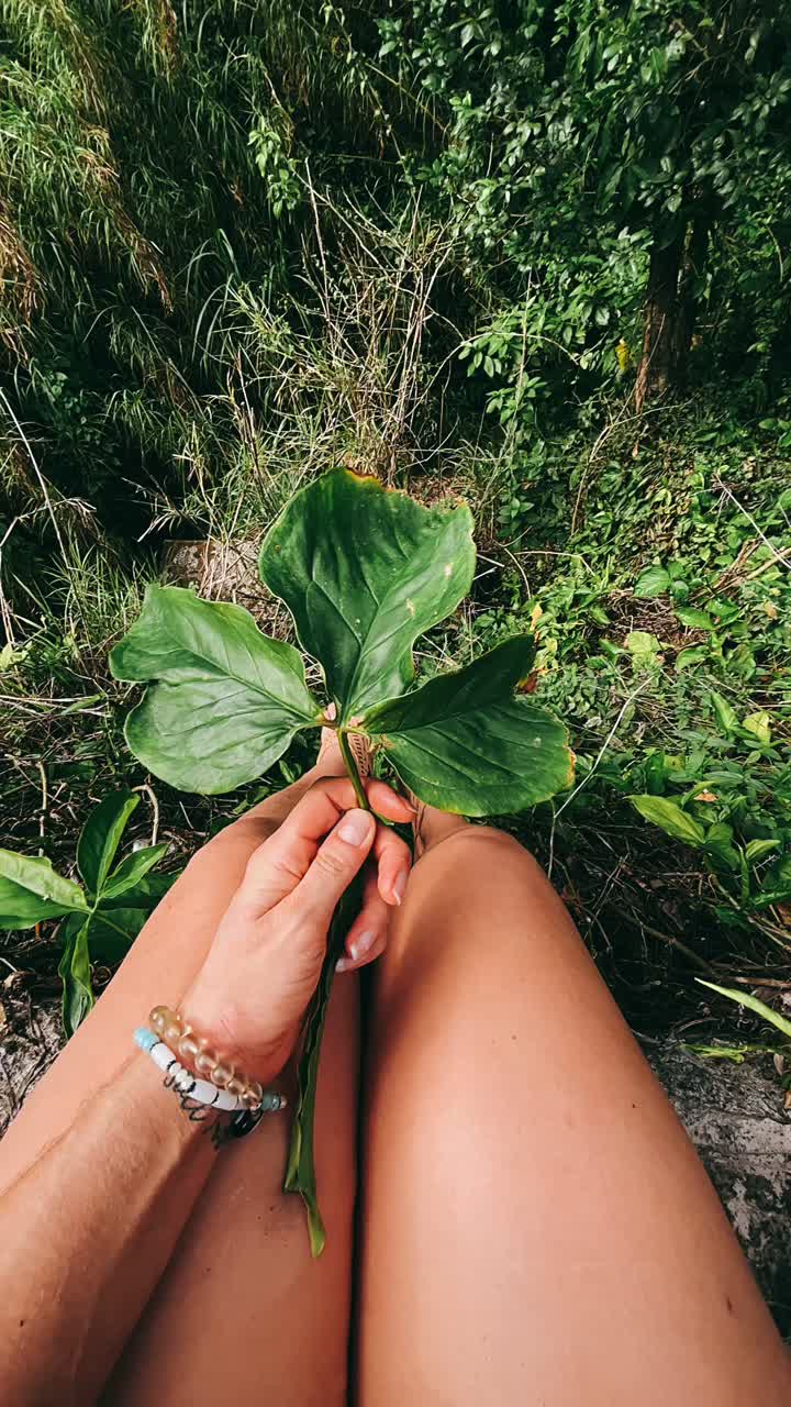 Woman holding a large green leaf in a forest