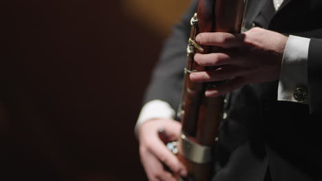 un hombre está tocando el fagot en una orquesta de metales vista de cerca de las manos del fagotista el músico está usando un instrumento de viento