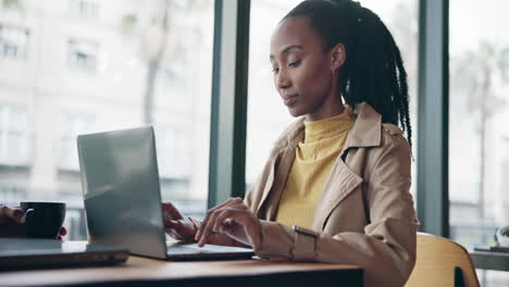 Black woman typing on laptop in coffee shop