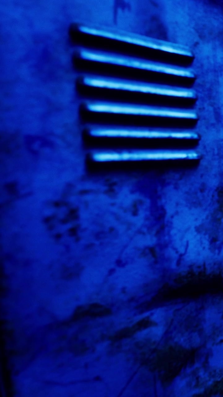 Superfície de metal com linhas de ventilação mostra desgaste e iluminação azul à noite.