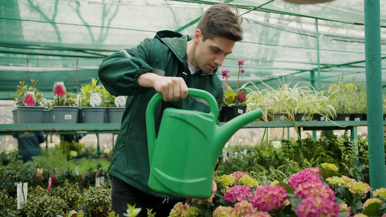 Un ragazzo in un'uniforme verde speciale innaffia i fiori con un righello verde in un negozio di fiori specializzato.