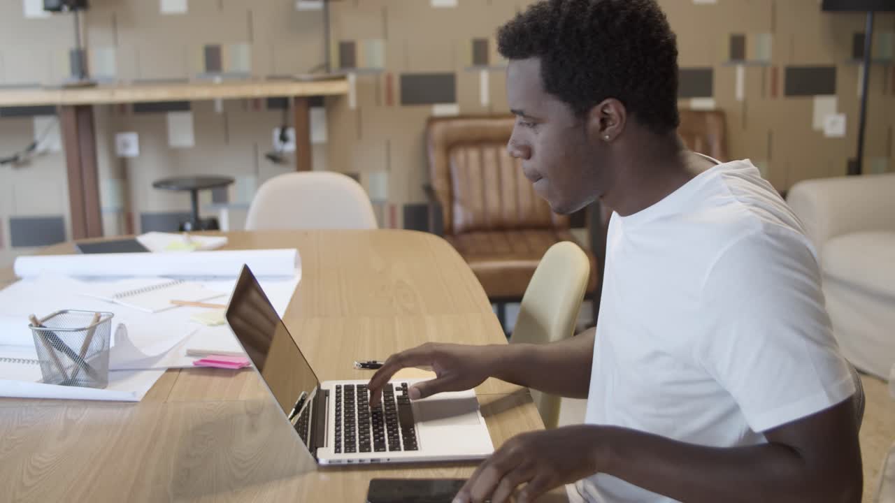 African American manager stops talking on phone, checks info on the laptop and writes a note