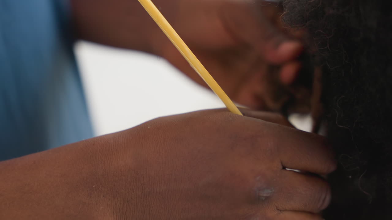 Primo piano di mani che avvolgono capelli neri attorno a un pettine giallo, sezionatura attenta e presa salda mostrano una tecnica meticolosa, ricci di media lunghezza rivelati, movimento concentrato, ritmo concentrato, atmosfera da studio di salone.
