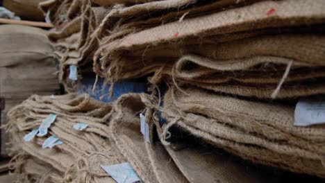 Well-worn-used-natural-hessian-jute-coffee-sacks-with-red-writing-stacked-up-in-a-coffee-production-warehouse