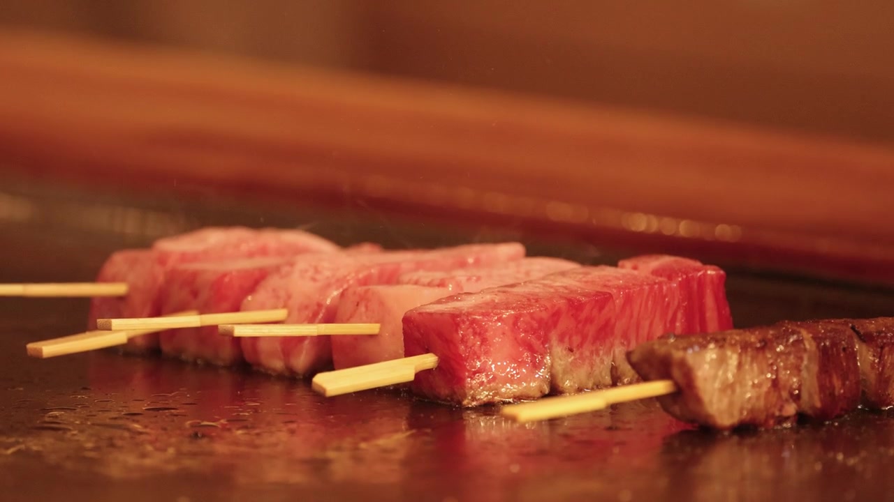 Primo piano di spiedini di manzo wagyu marmorizzato che sfrigolano su una calda griglia teppanyaki a Tokyo