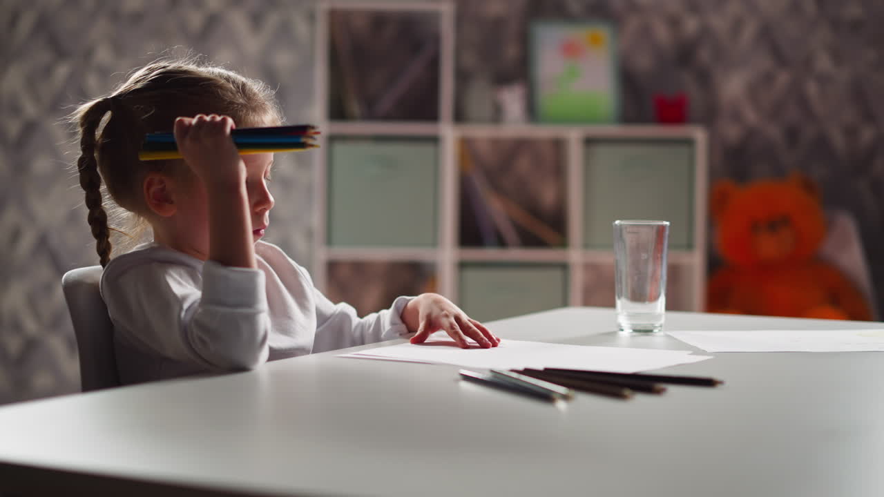 маленький художник поворачивает бумагу и рисует картинку карандашами