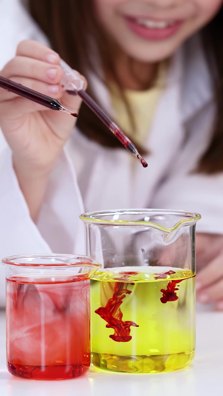 Close-up of a student using a pipette to drop red liquid into a yellow solution.