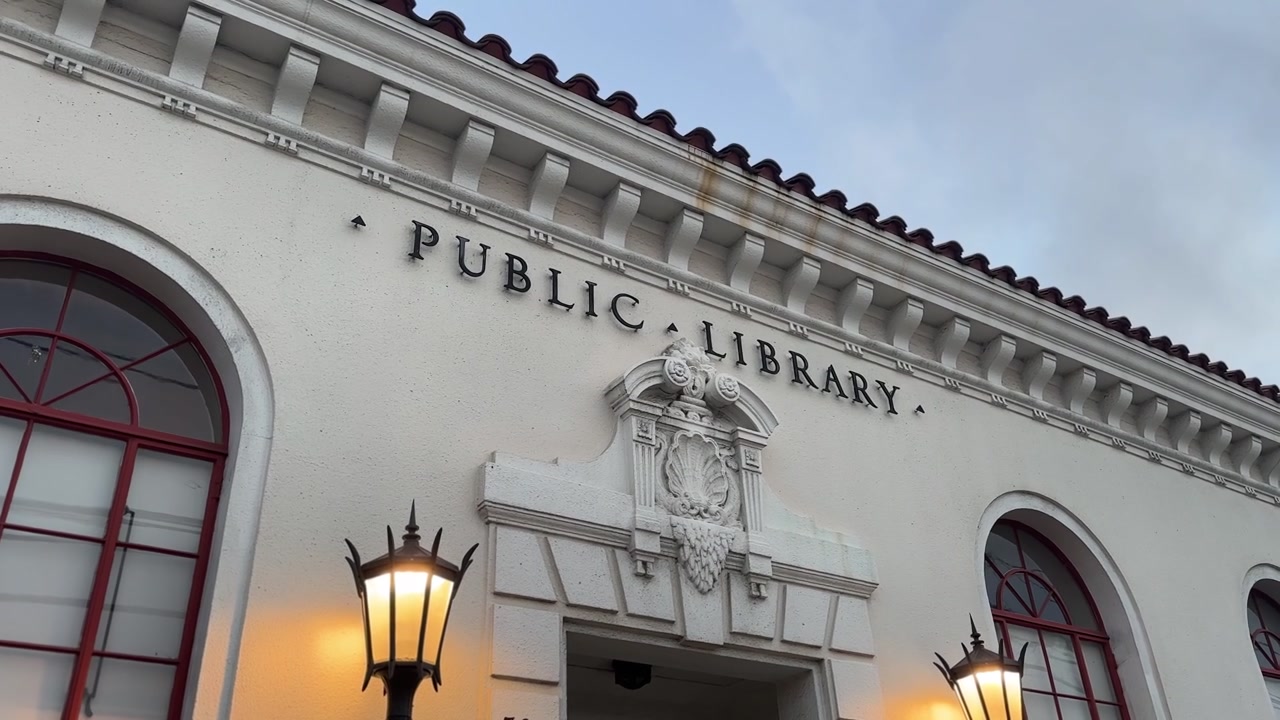 Ampia inquadratura serale della facciata della Biblioteca Pubblica di West End ad Alameda, California, con lampioni in ferro vintage, dettagli in stile neospagnolo, finestre ad arco e una morbida illuminazione crepuscolare. Telecamera statica.