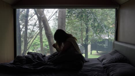young woman stretching after waking up in bed, with a nature view outside the window