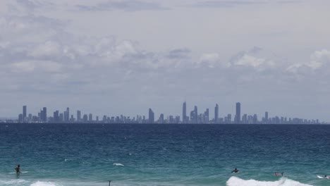 surfers catching waves with city skyline backdrop